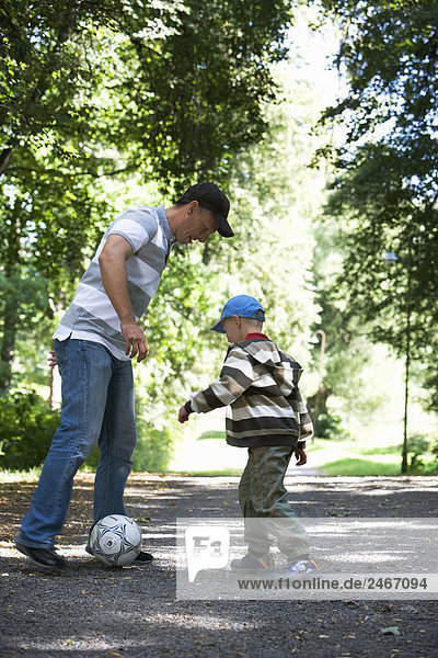 Vater und Sohn spielen Fußball in einem Park am sonnigen Tag Schweden.