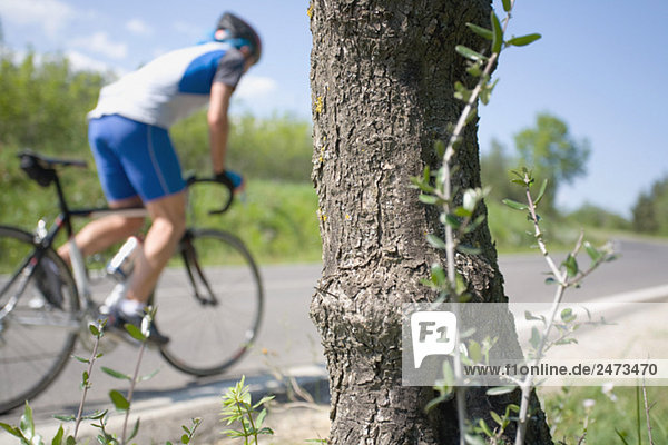 Radfahrer Radsport auf Straße mit Baumrinde im Vordergrund