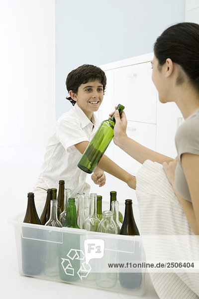 Junge Frau und Junge stellen Glasflaschen in den Papierkorb und lächeln sich an.