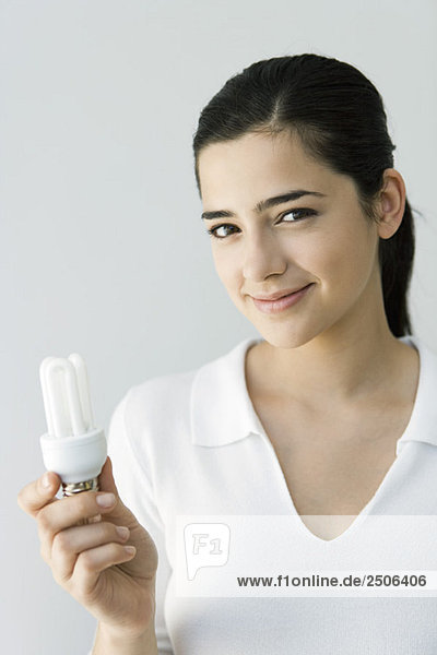 Young woman holding energy efficient light bulb  smiling at camera