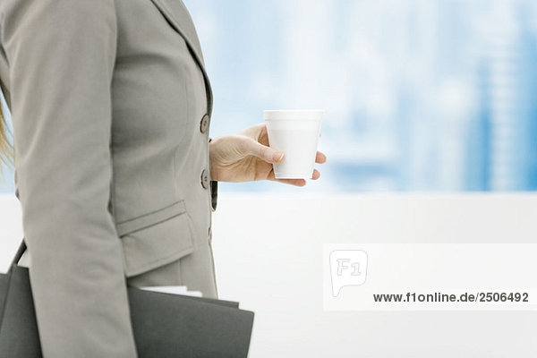 Businesswoman holding disposable coffee cup and briefcase  cropped side view