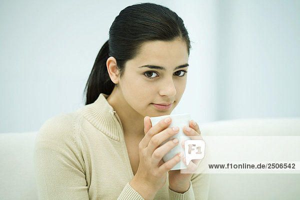 Young woman sitting  holding coffee mug  smiling at camera
