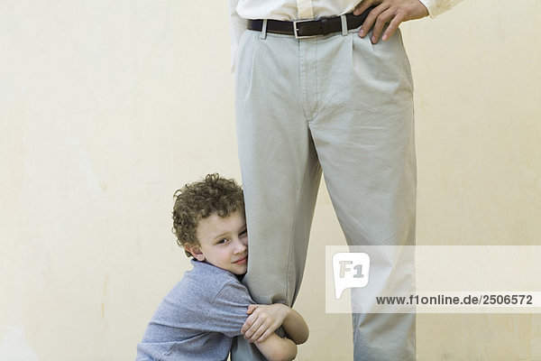 Junge klammert sich an das Bein seines Vaters  schaut in die Kamera  Blick in den Ausschnitt