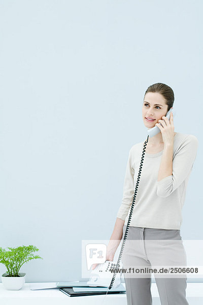 Frau steht und redet am Festnetztelefon  schaut weg und lächelt