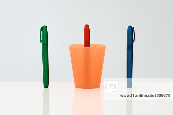 Stifte stehen aufrecht in einer Reihe  der mittlere Stift verkehrt herum in der Tasse