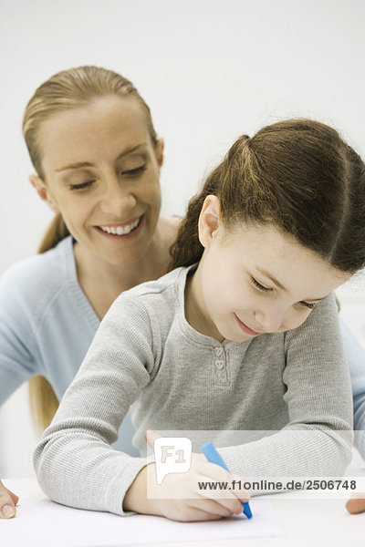 Girl drawing with crayon  mother looking over her shoulder and smiling