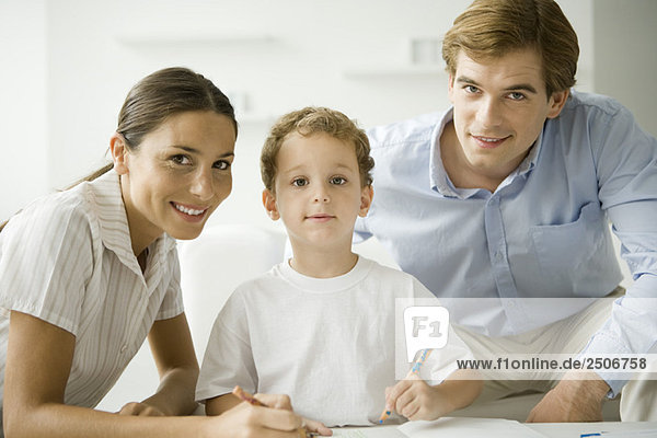 Little boy sitting with parents  drawing with pencil  all smiling at camera