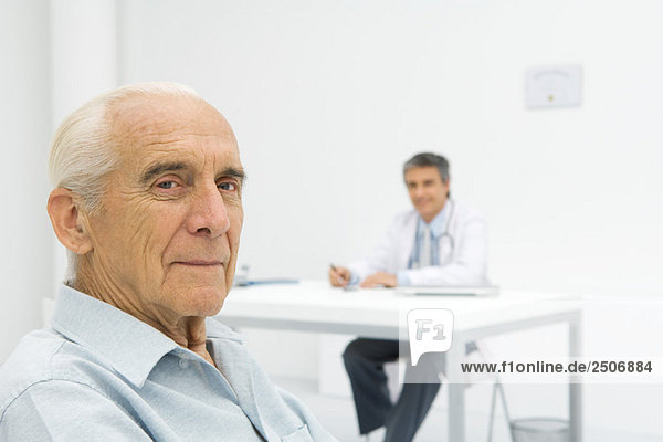 Doctor working at desk  focus on senior patient in foreground