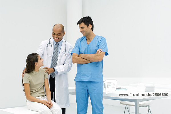 Doctor standing with hands on teen girl's shoulders  male nurse standing nearby