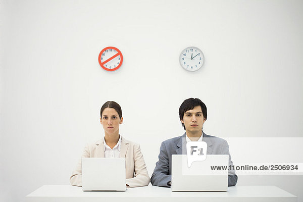 Büroangestellte sitzen unter der Uhr  benutzen Laptops  Warnschild über einer Uhr