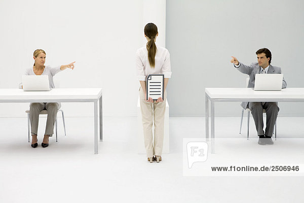 Büroangestellte  die an Schreibtischen sitzen und beide auf eine Frau zeigen  die das Dokument hinter ihrem Rücken hält.