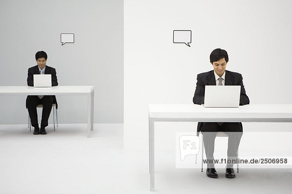 Junge Profis sitzen am Schreibtisch  benutzen Laptops  leere Wortblasen über den Köpfen