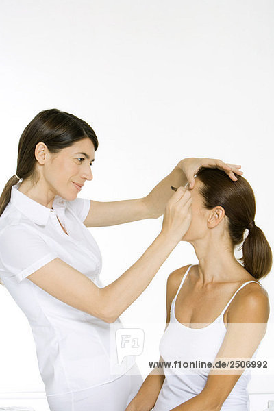 Beautician carefully plucking a woman's eyebrows  smiling