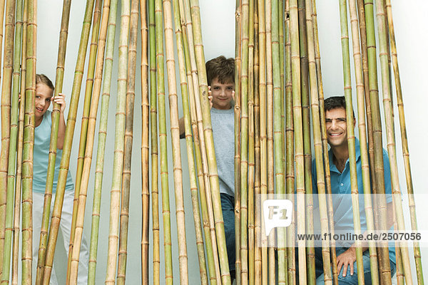 Vater und zwei Kinder schauen durch den Bambus in die Kamera  alle lächelnd.