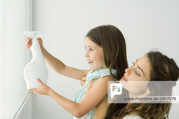 Kleines Mädchen putzt Fenster  Mutter hält sie  beide lächelnd