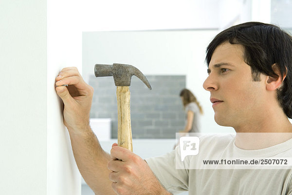Man hammering nail into wall  woman in background