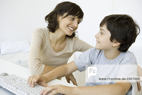 Mutter und Sohn sitzen und lächeln sich an  Junge mit Tastatur