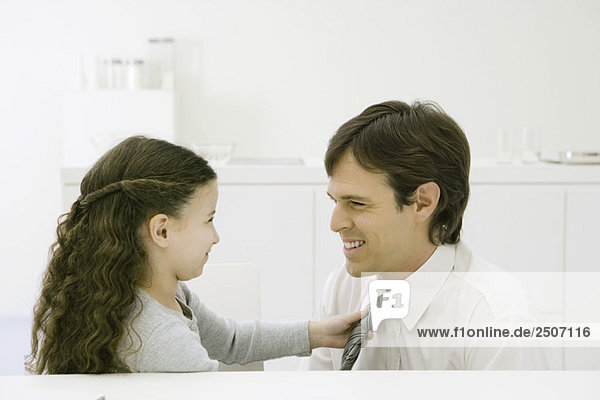 Little girl adjusting her father's tie  both smiling at each other