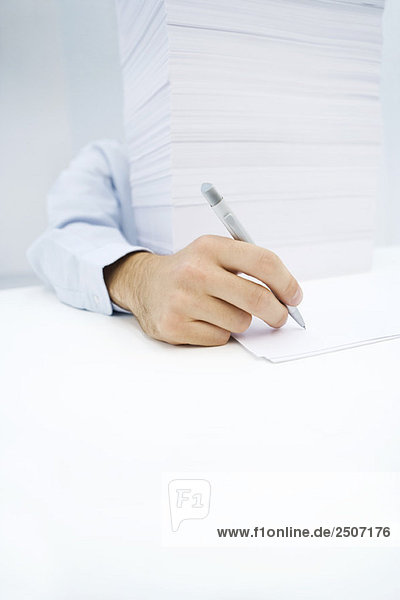 Arm  der um einen massiven Papierstapel greift  um auf ein einzelnes Blatt zu schreiben.