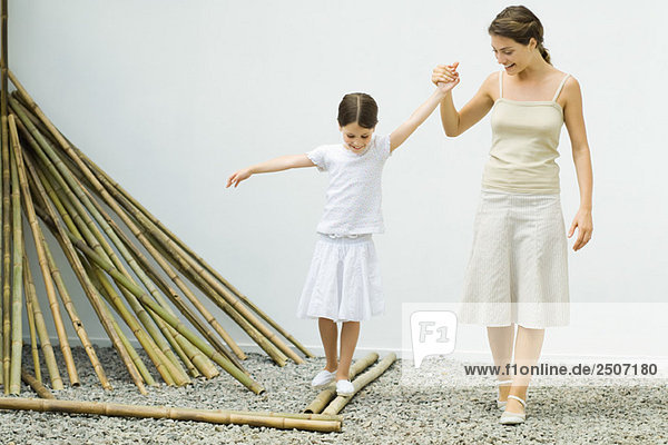 Mädchen balanciert auf Bambus  Mutter hilft ihr  indem sie ihre Hand hält.