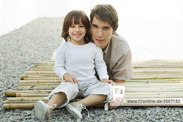 Junger Mann und Sohn auf Bambus zusammen  beide lächelnd vor der Kamera