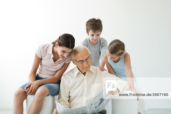 Großvater liest Zeitung  drei Enkelkinder schauen ihm über die Schulter.