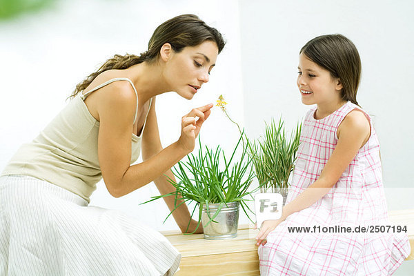 Frau riecht Blumenzweig  während Tochter zuschaut