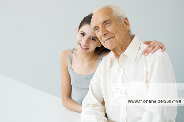 Teenage girl with arm around her grandfather's shoulder  senior man looking away