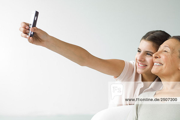 Teenage girl photographing self and grandmother with cell phone  both smiling