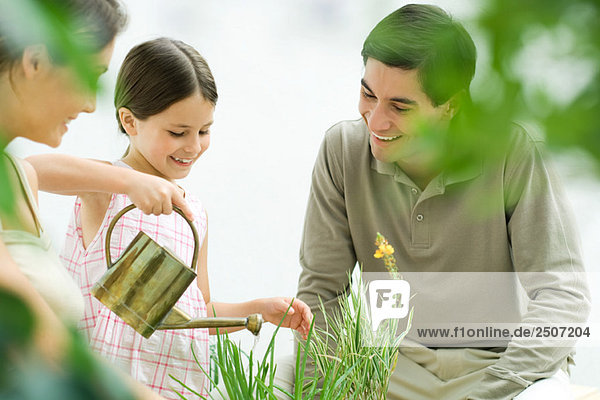 Mädchen gießen Pflanzen  Eltern beobachten  alle lächeln