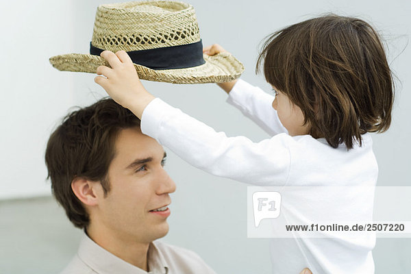Kleiner Junge  der den Hut vom Kopf seines Vaters aufhebt.