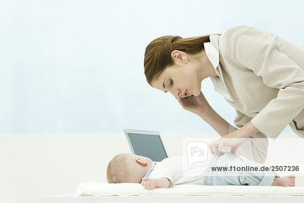 Professionelle Frau im Büro  mit dem Handy  Bücken über Baby auf dem Schreibtisch
