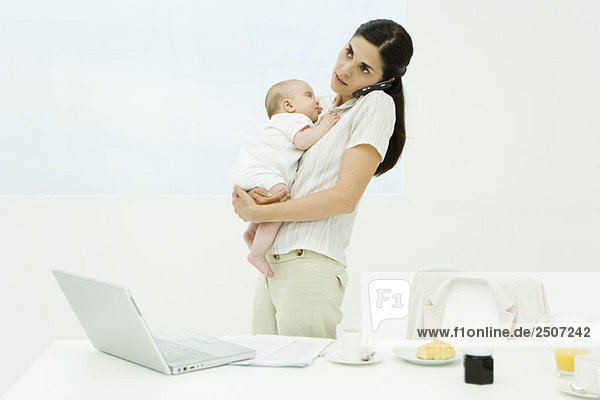 Professionelle Frau am Frühstückstisch stehend  Baby haltend  Handy benutzend