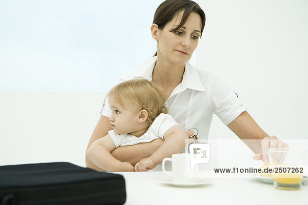 Professionelle Frau sitzt am Frühstückstisch und hält Kleinkind und Schlüssel.