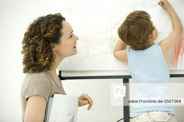 Professionelle Mutter mit Dokumenten  die die Farbe des Sohnes mit Buntstift beobachtet.