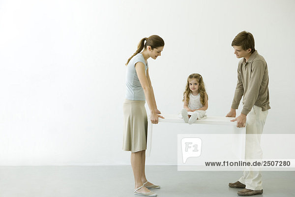 Young couple carrying table with daughter sitting on it