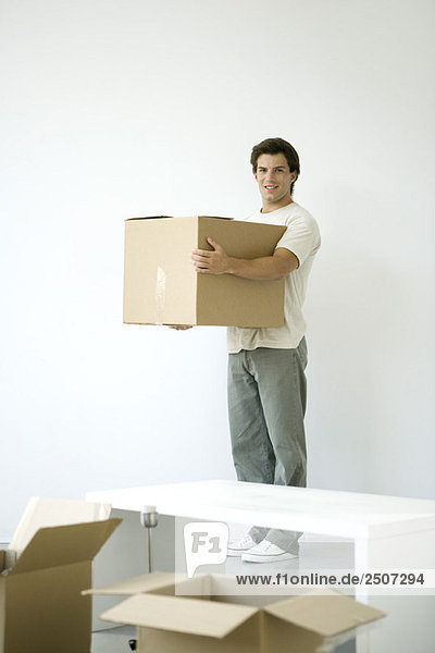 Man holding cardboard box  smiling at camera  opened boxes in foreground
