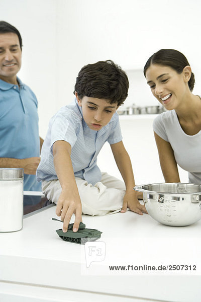 Junge spielt mit Spielzeugtank auf der Küchentheke  Eltern schauen zu und lächeln