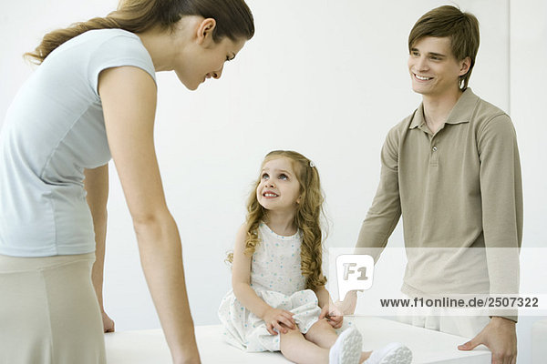 Young parents holding table  daughter sitting on table  smiling