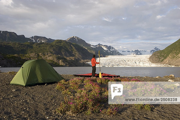 Kayaker standing near tent on shoreline of Grewingk Glacier Lake w/glacier in background Kenai Peninsula