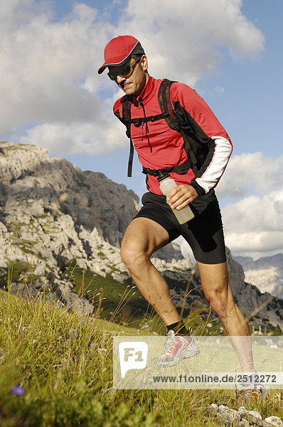 Male athlete in sportswear running up a grassy hill in Trentino  Southern Tyrol  in the background the Dolomites