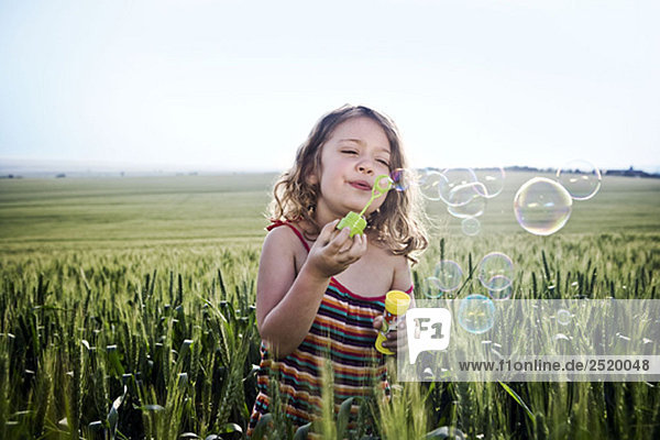 Mädchen bläst Blasen im Weizenfeld