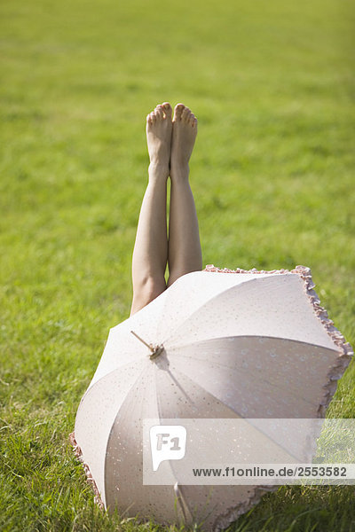 Junge Frau im Gras liegend  hinter einem Regenschirm