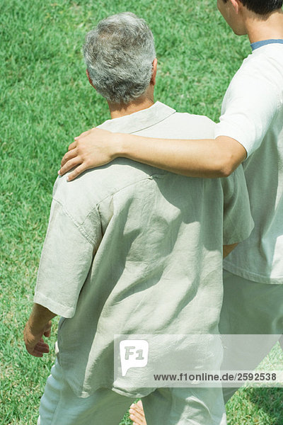 Young man with his arm across the shoulder of an older man walking together across grass