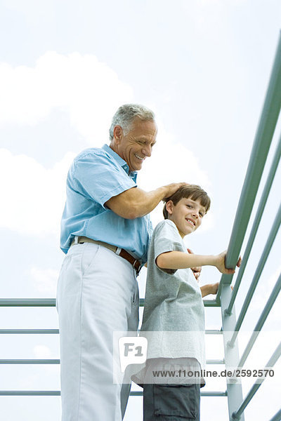 Senior man with grandson on balcony  his hand on his head  both smiling