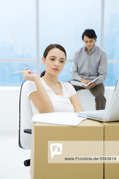 Young woman sitting at cardboard box desk  looking at laptop computer