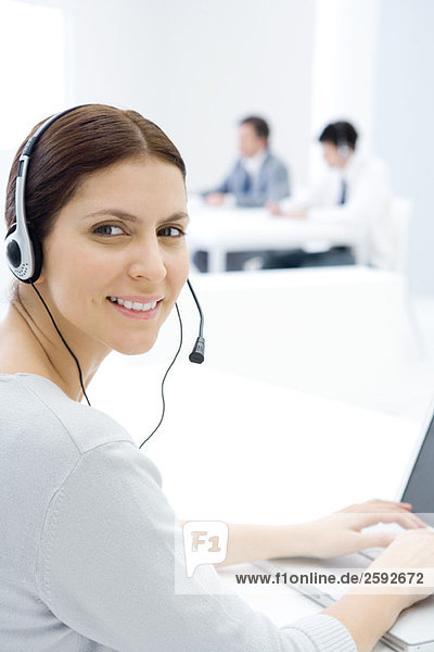 Woman wearing headset  working at desk  smiling over shoulder at camera