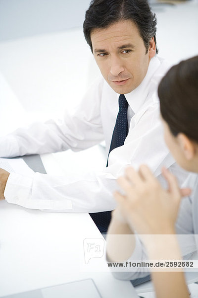 Professional man sitting at desk  talking with female colleague  high angle view