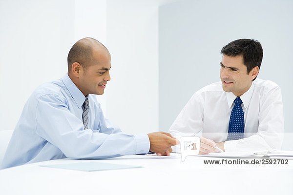 Zwei Geschäftsleute sitzen am Tisch und diskutieren über ein Dokument.