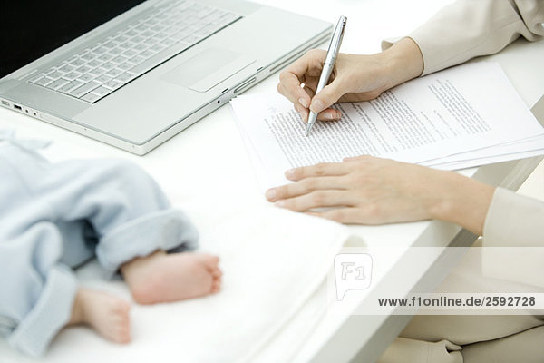 Frau redigiert Dokument am Schreibtisch  Kleinkind liegt in der Nähe  Schnittansicht
